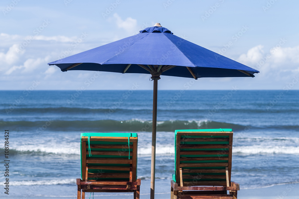 Blue umbrella with two recliners at the ocean coast