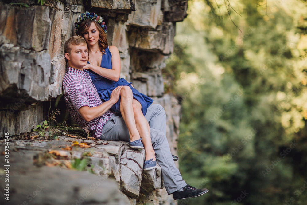 Young beautiful tender modern stylish couple of slim woman and man sitting on rock with near big stony grey wall on outdoor Young beautiful tender modern stylish couple of slim woman and man sitting on rock with near big stony grey wall on outdoor