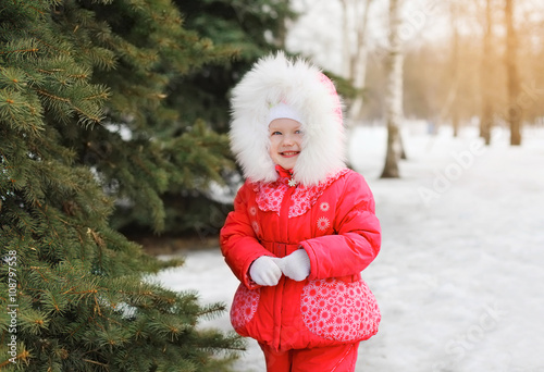 Child walking in winter forest near christmas tree