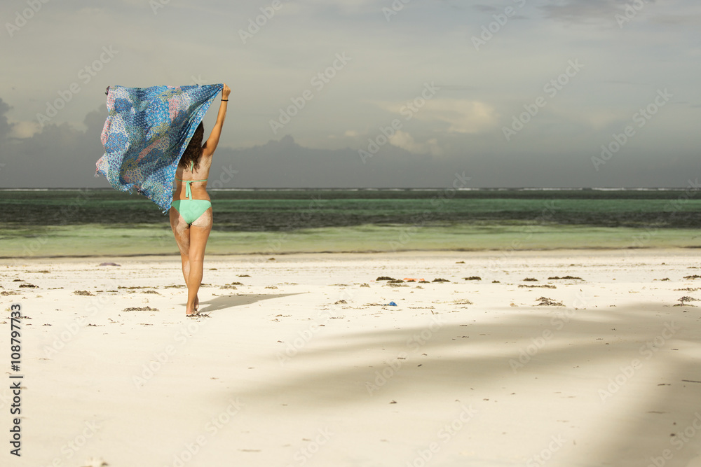 Portrait of young woman wearing a blue sarong and bikini on the tropical beach
