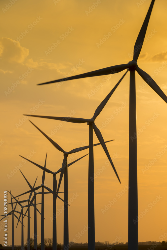 Obraz premium Windmill wind turbine generating power turning silhouetted against sunset sky