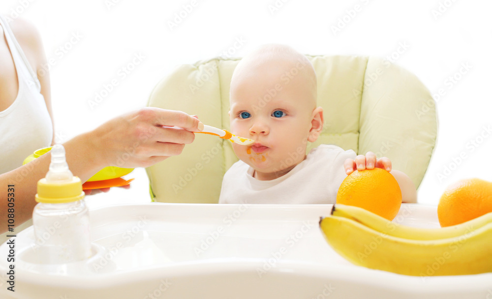 Mother feeds baby spoon on the table at home