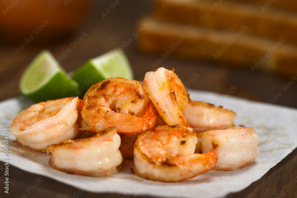 Fresh fried shrimps with lime wedges on sandwich paper with toast bread slices in the back (Selective Focus, Focus one third into the shrimps) Fresh fried shrimps with lime wedges on sandwich paper with toast bread slices in the back (Selective Focus, Focus one third into the shrimps)