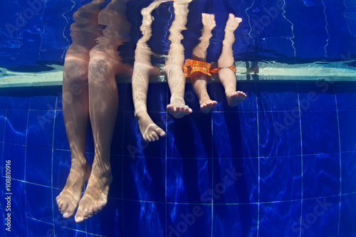 Happy people relaxing with fun. Funny underwater photo mother with kids legs in aqua park swimming pool. Family lifestyle and summer children water sports activity and lessons with parents on vacation