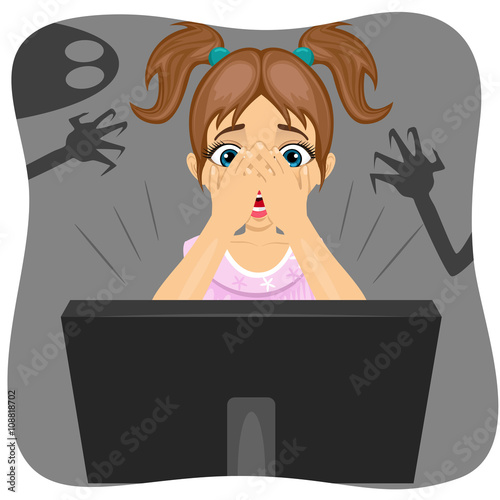 little girl covering her face while watching horror movie on internet.  Shadow of ghost on wall