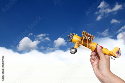 woman's hand holding toy airplane against blue sky