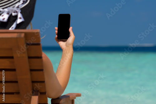 Young girl lying on a beach lounger with mobile phone in hand on