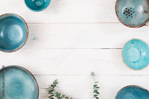 Many turquoise clay empty plates and free space in center on a white wooden background. Top view on set of trendy handmade empty plates. Organic food, healthy life, pottery, decoration concept