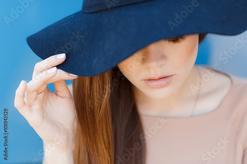 Young beautiful woman brunette with long straight hair and brown eyes,dressed in a beige blouse with short sleeves, wears a dark blue hat with large brim, poses in the summer outdoors