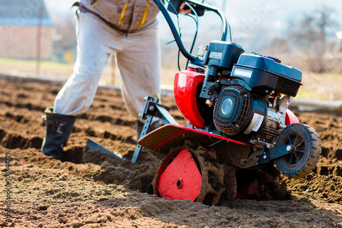 Man working in the garden with Garden Tiller. Garden tiller to work, closeup. Man with tractor cultivating field at spring photo