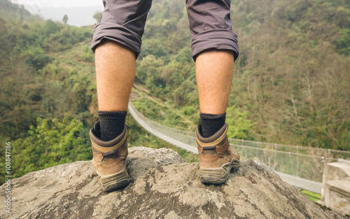 Hiker legs standing on rock above mountain suspension bridge 