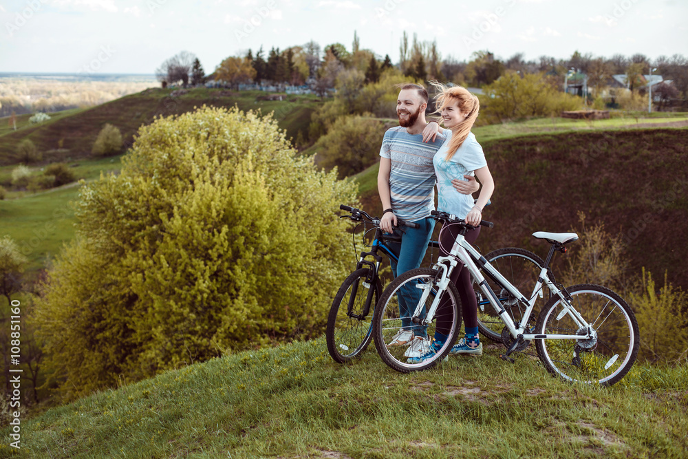 Beautiful young couple in love walking with bicycles,standing and hugging near the Bicycle and consider nature. The concept of active rest