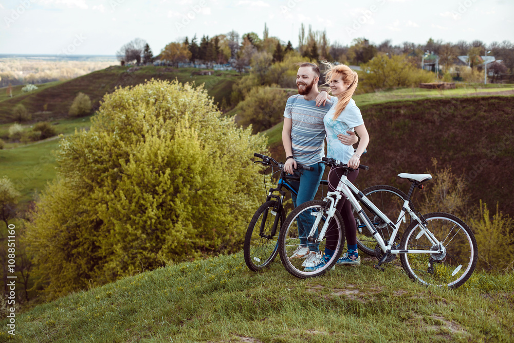 Fototapeta premium Beautiful young couple in love walking with bicycles,standing and hugging near the Bicycle and consider nature. The concept of active rest