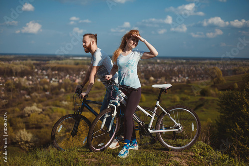 Fototapeta Naklejka Na Ścianę i Meble -  Beautiful young couple in love walking with bicycles, looking towards the beautiful nature and the blue sky. The concept of active rest