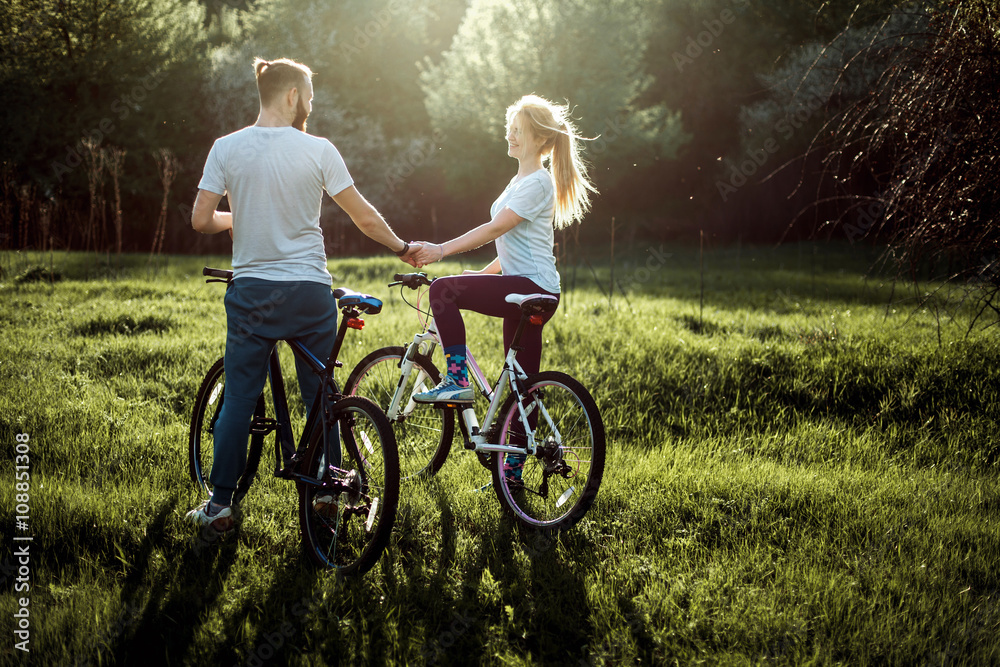 Fototapeta premium Beautiful young couple in love walking with bicycles, holding hands and talking. Stand near the bikes. The concept of active rest
