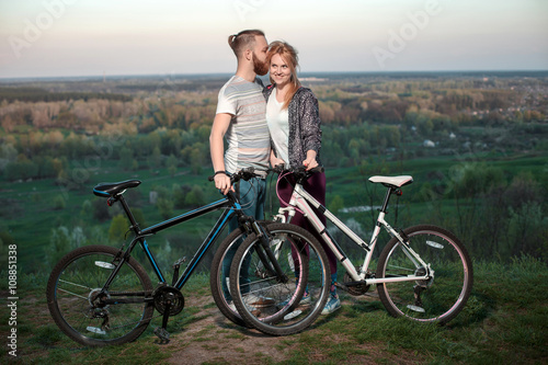 Beautiful young loving couple hugging at sunset, there are two bikes. The concept of happiness, peace and love