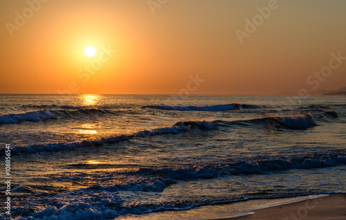 Sunrise over the sea  the rolling calm waves  sandy beach. Skay orange  waves blue.