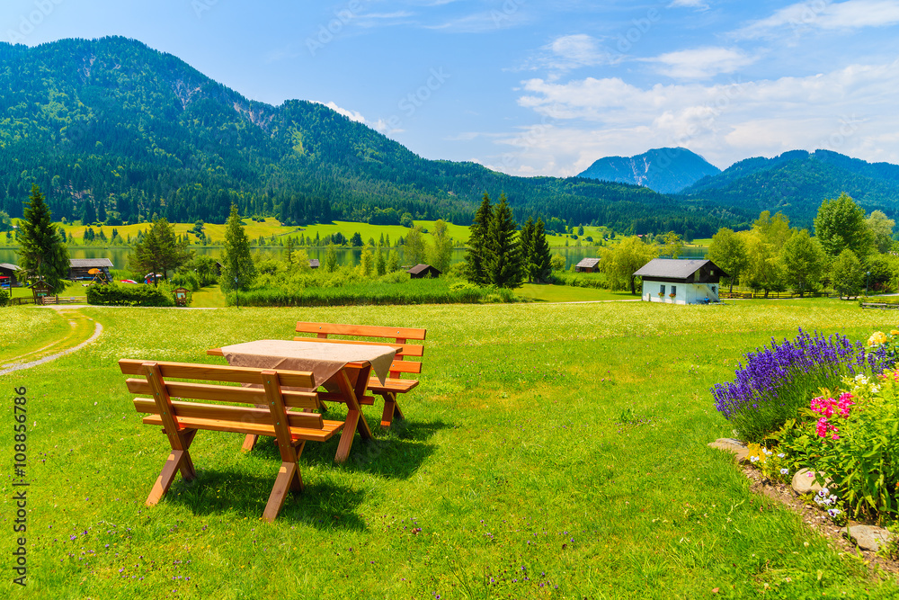 Benches with picnic table on green grass in alpine village on shore of Weissensee lake in summer landscape of Alps Mountains, Austria Benches with picnic table on green grass in alpine village on shore of Weissensee lake in summer landscape of Alps Mountains, Austria