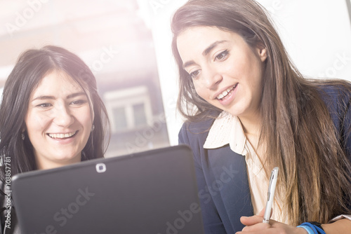 Young successful business women discussing and sharing ideas, using tablet in bright modern office. Focus on girl on the right