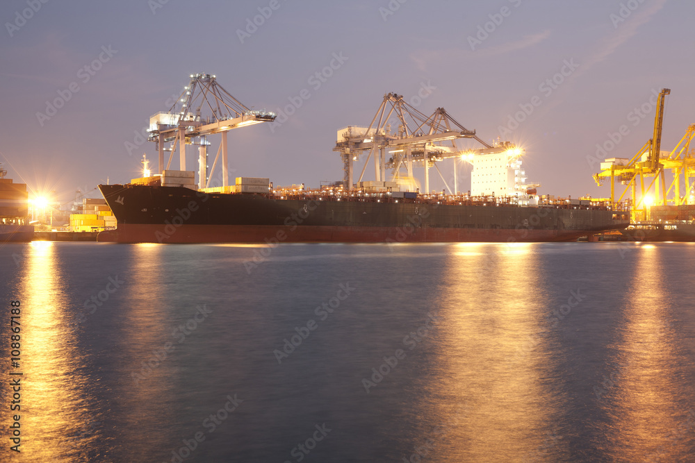 Fototapeta premium Big ship in harbour using cranes loading containers in night time