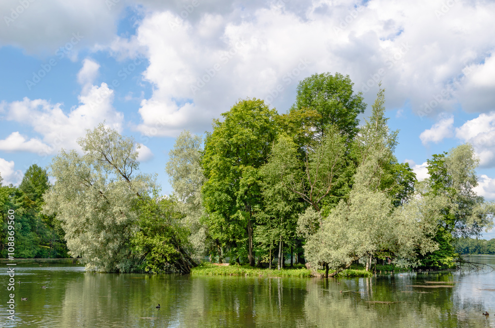 Small island with silvery willows in the midst of a beautiful lake against the blue sky and the Gatchina Palace near Saint Petersburg. Small island with silvery willows in the midst of a beautiful lake against the blue sky and the Gatchina Palace near Saint Petersburg.