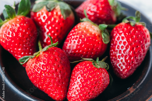   Whole red ripe strawberries in a black bowl on a white background