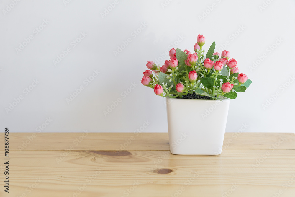 the artificial flower in the white pot on the wooden table with