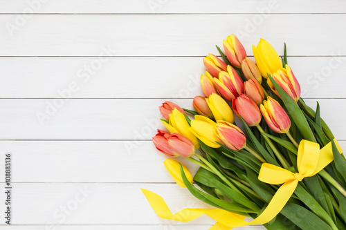 Bouquet of yellow tulips decorated with yellow ribbon on white wooden background. Copy space, top view 