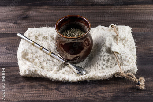 Yerba mate in ceramic matero with bombilla on linen bag on wooden table. photo