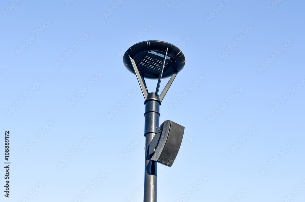 Street lamp with the speaker in blue sky in mont-royal park next to beaver lake, Montreal, Canada.