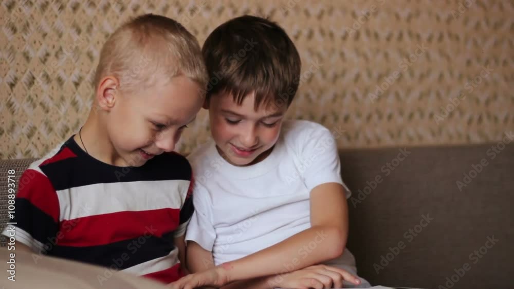 Two boys sitting on a couch and read a book smiling Two boys sitting on a couch and read a book smiling