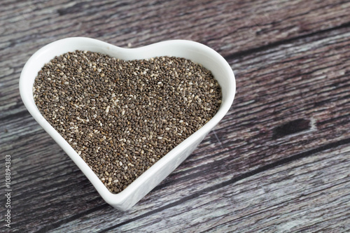Chia seed in heart-shaped bowl on a wooden table.