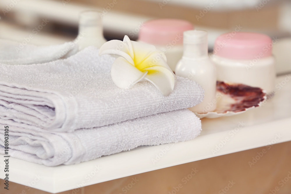 White towels with cream and tropical flower on a shelf in bathroom White towels with cream and tropical flower on a shelf in bathroom