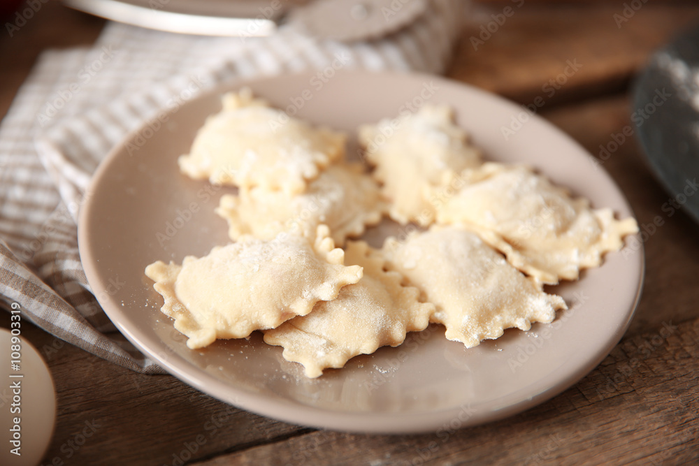 Uncooked ravioli on plate on wooden table
