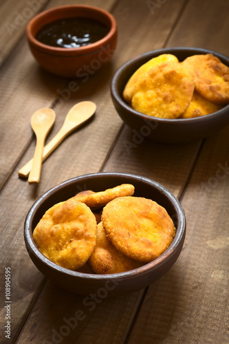 Traditional Chilean Sopaipilla fried pastry made of mashed pumpkin, served with Chancaca sweet sauce, photographed with natural light (Selective Focus, Focus on the first sopaipillas)