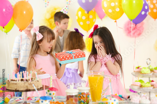Happy little girl presenting a gift to her friend at birthday party