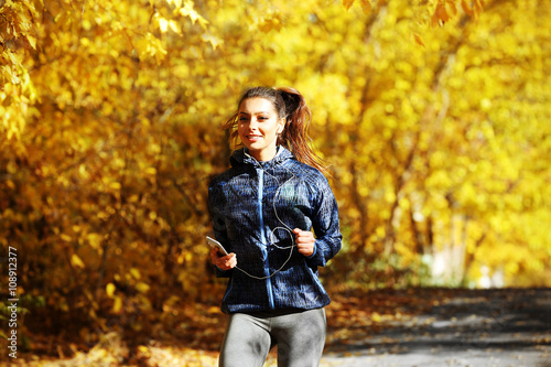Young beautiful woman running in autumn park and listening to music with headphones. © Africa Studio