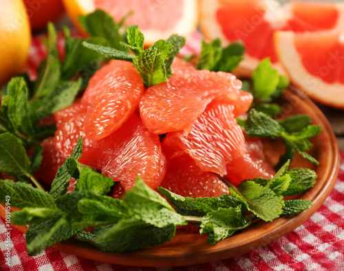 Juicy grapefruit pieces with fresh mint on a plate, close up