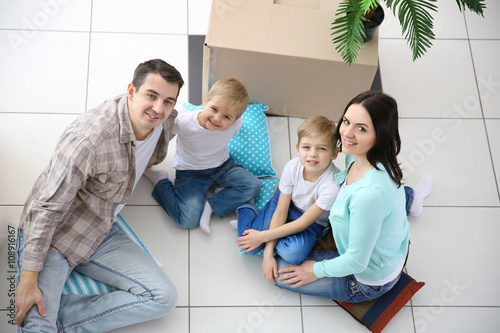 Moving concept. Happy family sitting on floor in new house with cardboard box  top view