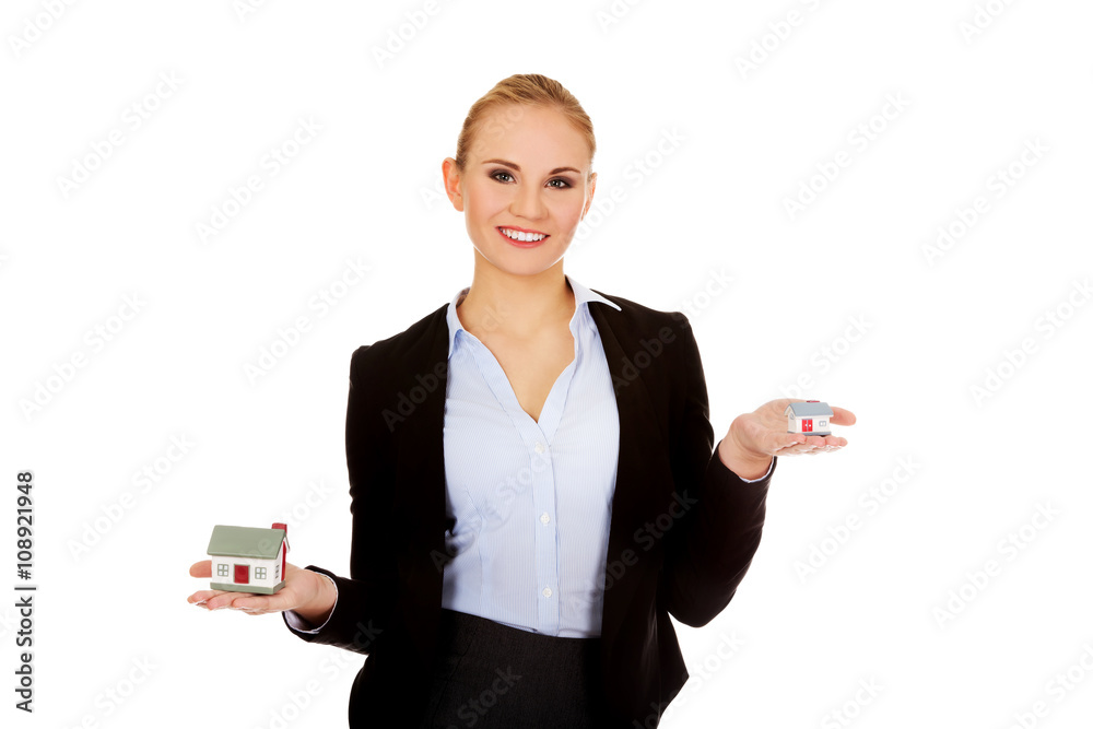 Smiling business woman compares two house models Smiling business woman compares two house models