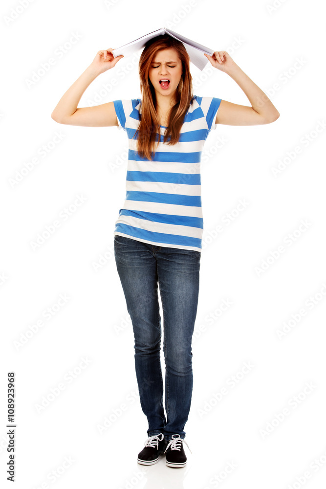 Screaming teenage woman with notebook on head Screaming teenage woman with notebook on head