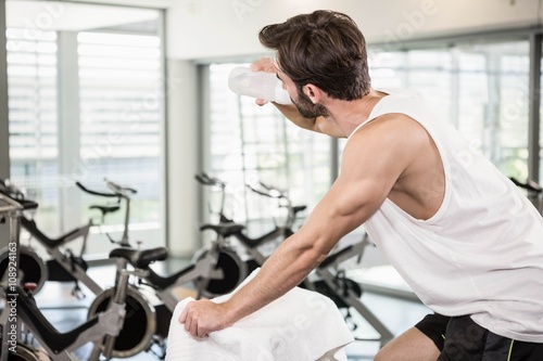 Fit man on exercise bike drinking water