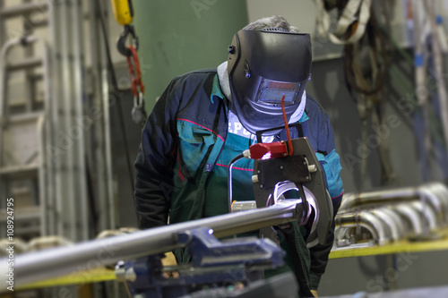 Industrial operator setting computer controlled process of orbital welding machine in inox pipes manufacturing workshop.