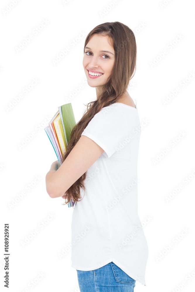 Side view of smiling female college student holding books while standing on white background