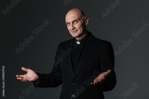 Smiling priest standing and inviting you photo