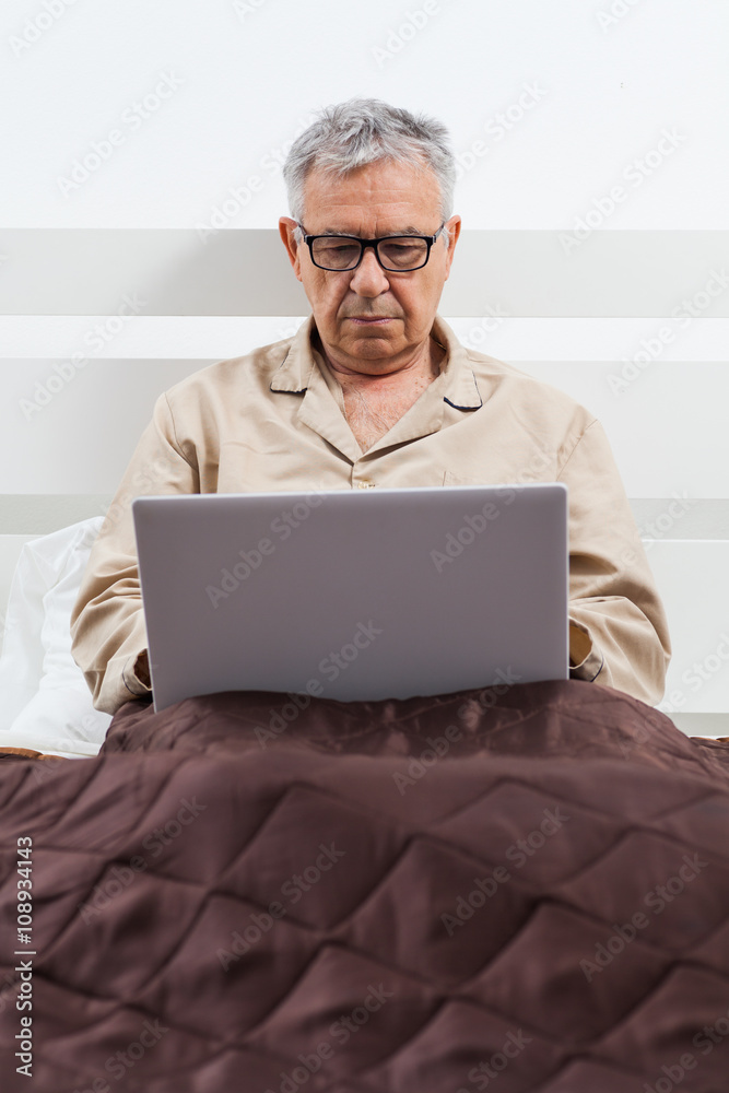 Senior man is lying in bed and using laptop Senior man is lying in bed and using laptop