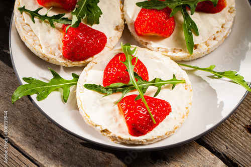 Multigrain rice cakes with strawberries fruit , soft mascarpone cheese and arugula for healthy breakfast.