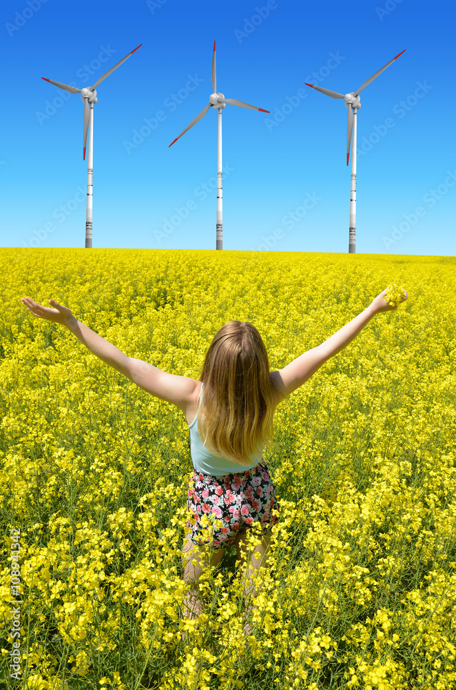 Young happy woman on blooming rapeseed field in the background wind turbines