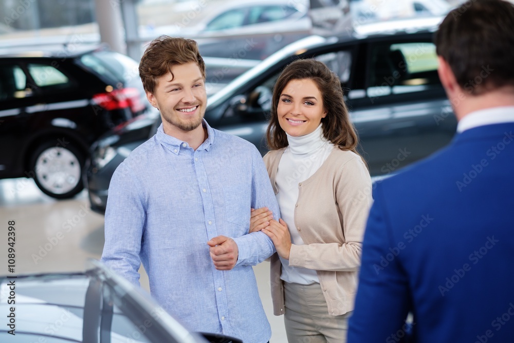 Salesman talking to a young couple at the dealership showroom. Salesman talking to a young couple at the dealership showroom.