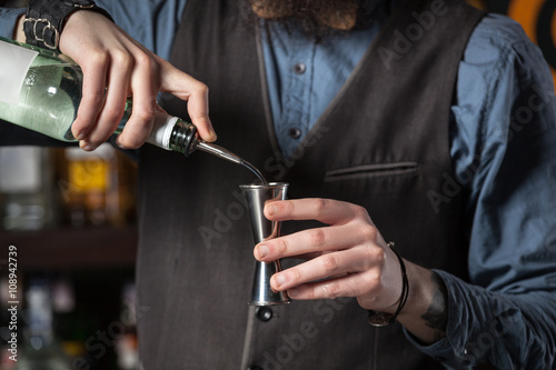 Barman pouring alcohol in the jigger. photo